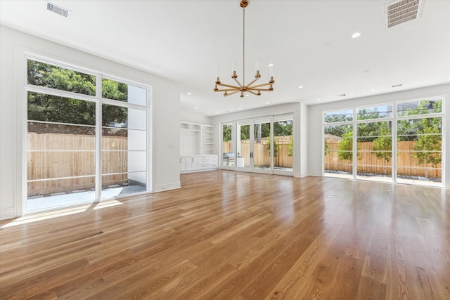 unfurnished living room featuring an inviting chandelier, built in shelves, and light hardwood / wood-style floors