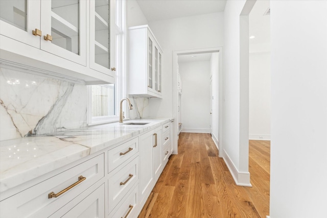 kitchen featuring light stone counters, white cabinets, light wood-type flooring, and sink