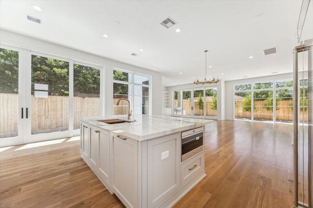 kitchen featuring light stone counters, sink, light hardwood / wood-style flooring, a kitchen island with sink, and white cabinetry