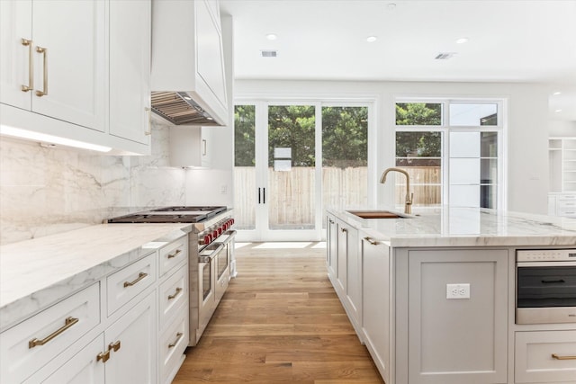 kitchen featuring backsplash, light stone countertops, stainless steel appliances, light hardwood / wood-style flooring, and sink