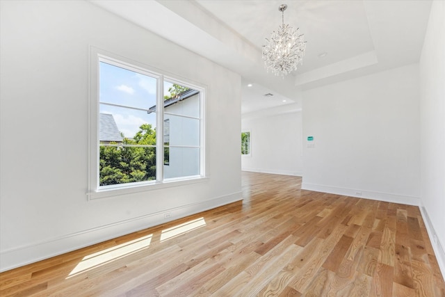 unfurnished room with an inviting chandelier, light hardwood / wood-style flooring, and a tray ceiling