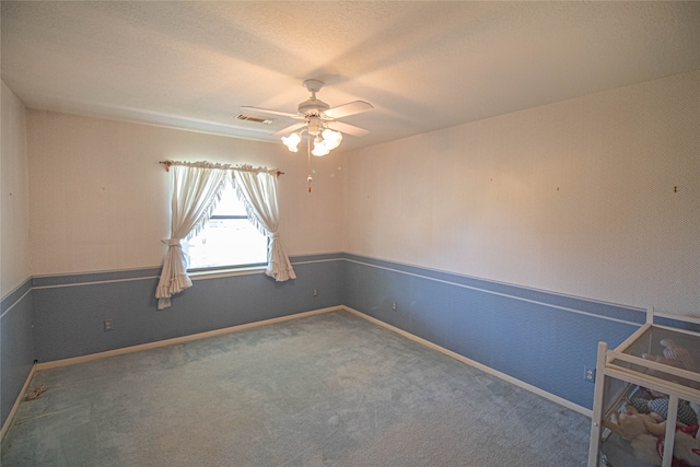 empty room featuring ceiling fan and dark colored carpet