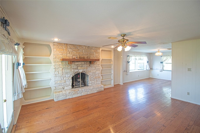 unfurnished living room featuring built in features, dark wood-type flooring, ceiling fan, and a fireplace