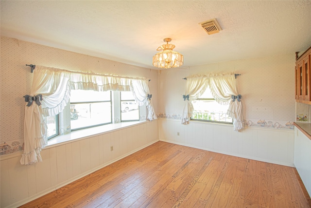 unfurnished room with light wood-type flooring, a wealth of natural light, and a chandelier