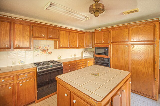 kitchen featuring black appliances, light tile floors, tile countertops, a kitchen island, and tasteful backsplash