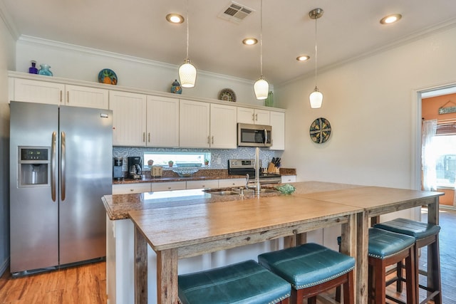 kitchen featuring pendant lighting, backsplash, stainless steel appliances, ornamental molding, and white cabinets