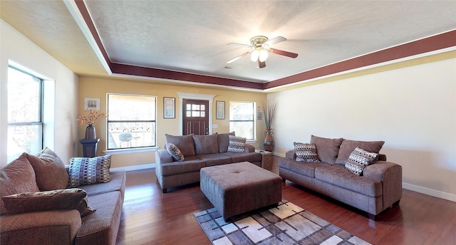 living area featuring ceiling fan, dark wood-style flooring, a raised ceiling, and baseboards