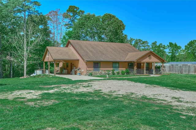 view of front of property with driveway, stone siding, roof with shingles, fence, and a front yard