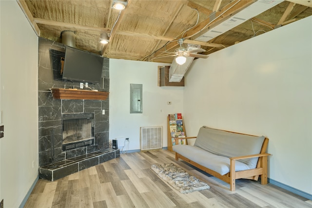 sitting room featuring tile walls, light wood-type flooring, a large fireplace, electric panel, and ceiling fan