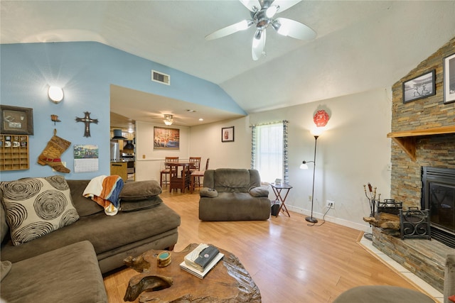 living area with light wood finished floors, visible vents, ceiling fan, vaulted ceiling, and a fireplace