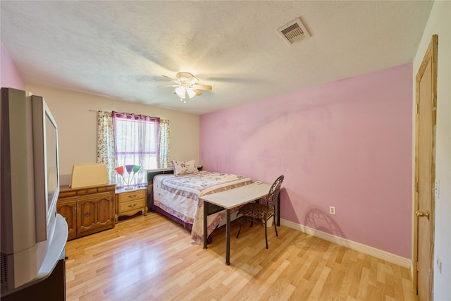 bedroom featuring visible vents, baseboards, a ceiling fan, light wood-style flooring, and a textured ceiling