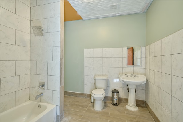 bathroom with tile walls, tiled shower / bath combo, and toilet