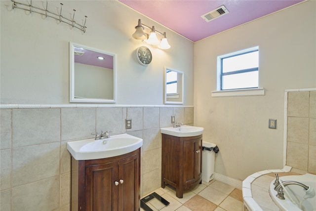 bathroom featuring tile walls, tile patterned floors, a bath, and dual vanity