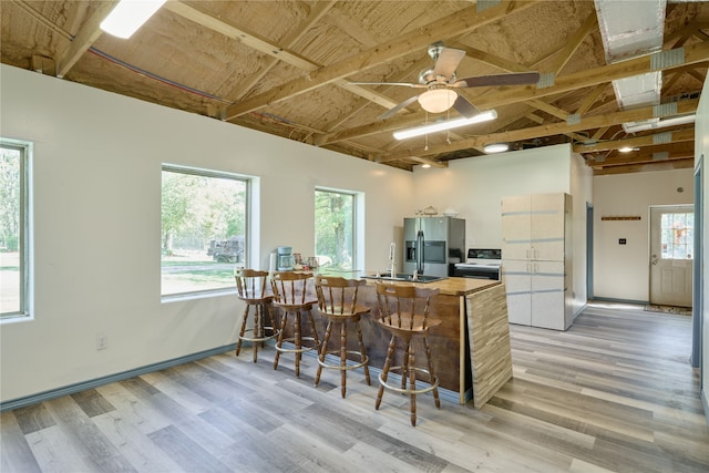 kitchen featuring light wood finished floors, range with electric cooktop, stainless steel fridge with ice dispenser, a breakfast bar area, and a peninsula