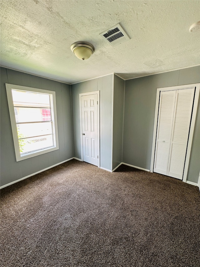 unfurnished bedroom featuring a textured ceiling and dark carpet