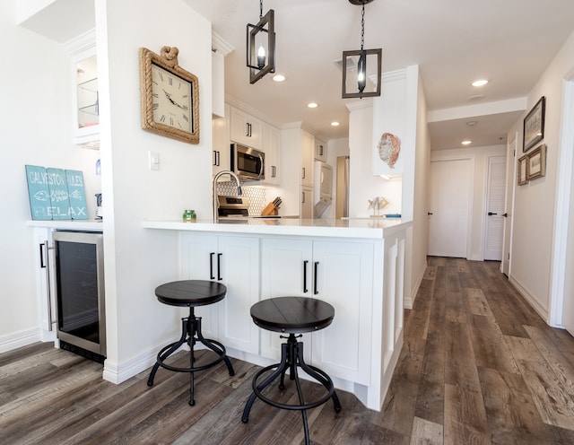 kitchen with beverage cooler, decorative light fixtures, kitchen peninsula, and dark hardwood / wood-style flooring