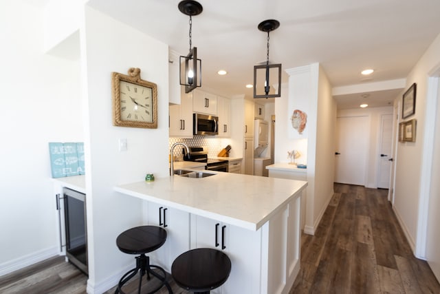 kitchen with appliances with stainless steel finishes, white cabinets, dark hardwood / wood-style floors, a kitchen bar, and hanging light fixtures