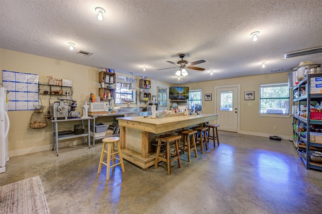 kitchen featuring a kitchen breakfast bar, a textured ceiling, concrete floors, and ceiling fan