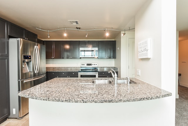 kitchen featuring dark brown cabinets, appliances with stainless steel finishes, sink, light stone counters, and track lighting