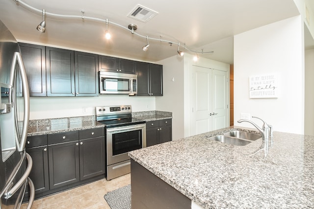 kitchen with light stone counters, stainless steel appliances, rail lighting, and sink