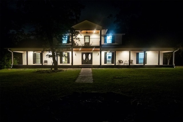 back house at twilight featuring a balcony and a yard