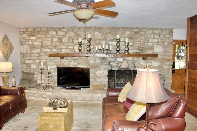 tiled living room featuring ceiling fan, a stone fireplace, and a textured ceiling