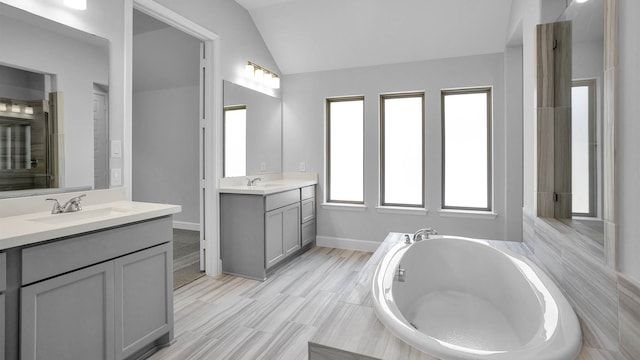 bathroom featuring double sink vanity, lofted ceiling, and tiled bath