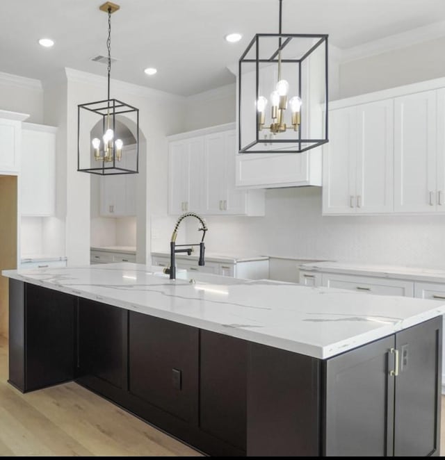 kitchen with decorative light fixtures, a notable chandelier, white cabinets, light hardwood / wood-style floors, and an island with sink