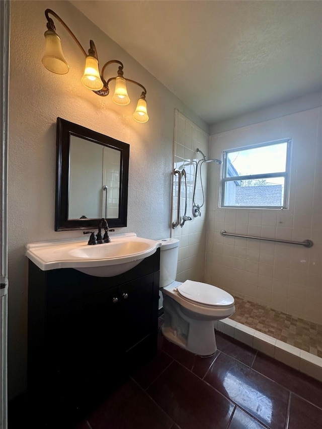 bathroom featuring a stall shower, a textured wall, toilet, tile patterned flooring, and vanity