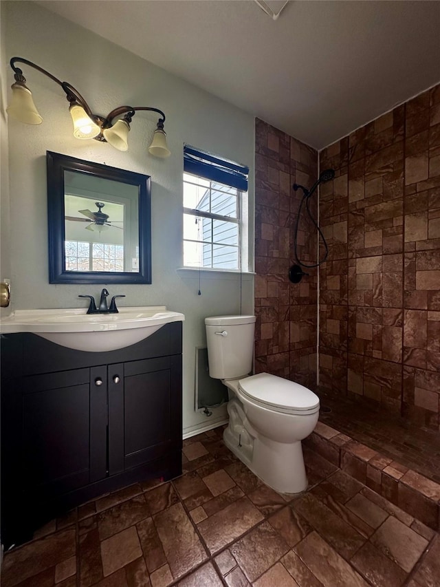 full bathroom featuring toilet, tiled shower, stone tile flooring, and vanity