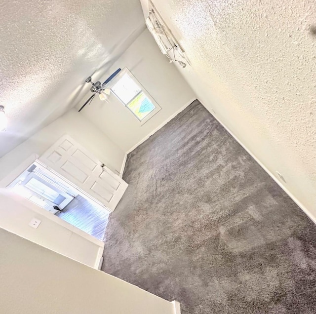 unfurnished living room with a textured ceiling, a textured wall, lofted ceiling, a ceiling fan, and dark carpet