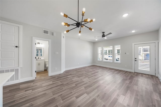 unfurnished living room featuring ceiling fan with notable chandelier and light hardwood / wood-style flooring