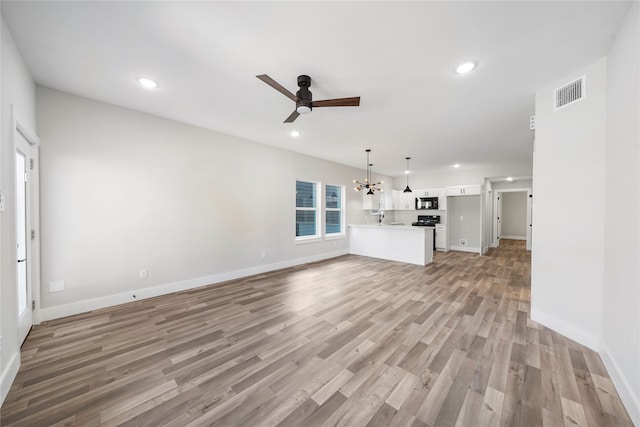 unfurnished living room with light wood-type flooring and ceiling fan with notable chandelier