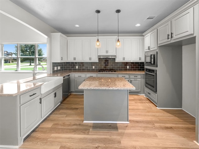 kitchen featuring light wood-type flooring, appliances with stainless steel finishes, light stone counters, white cabinetry, and a kitchen island