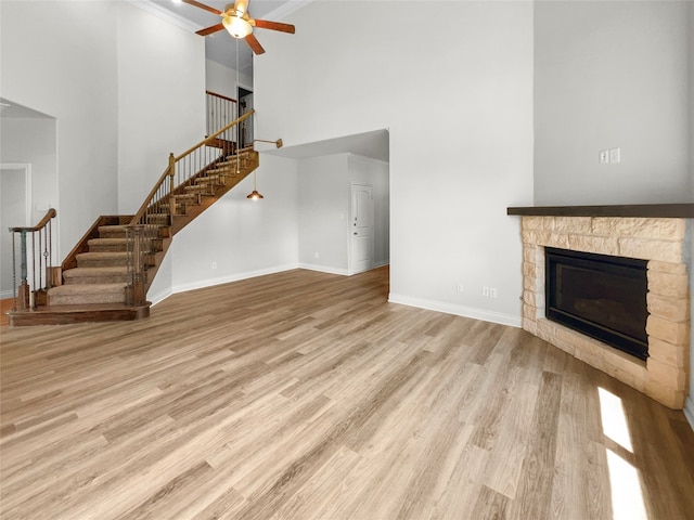 unfurnished living room with a fireplace, light wood-type flooring, a high ceiling, ornamental molding, and ceiling fan