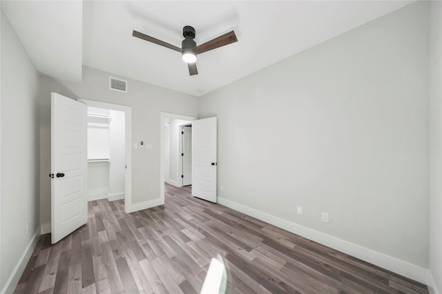 unfurnished bedroom with a walk in closet, wood-type flooring, and ceiling fan