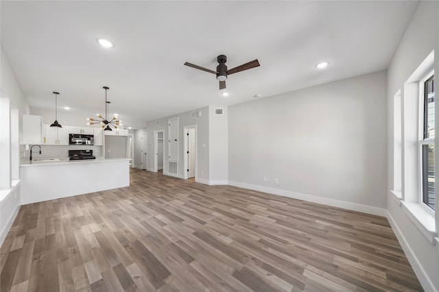 unfurnished living room with plenty of natural light, light hardwood / wood-style flooring, sink, and ceiling fan with notable chandelier