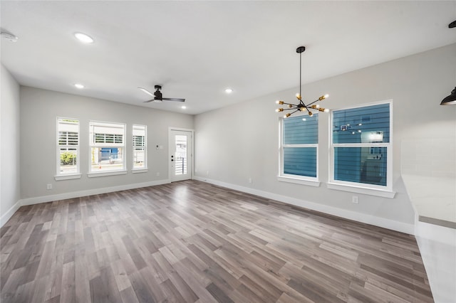 empty room featuring wood-type flooring and ceiling fan with notable chandelier