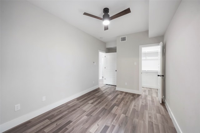 unfurnished bedroom with a spacious closet, a closet, ceiling fan, and hardwood / wood-style flooring