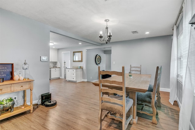 dining area featuring a notable chandelier, light wood-type flooring, and a textured ceiling