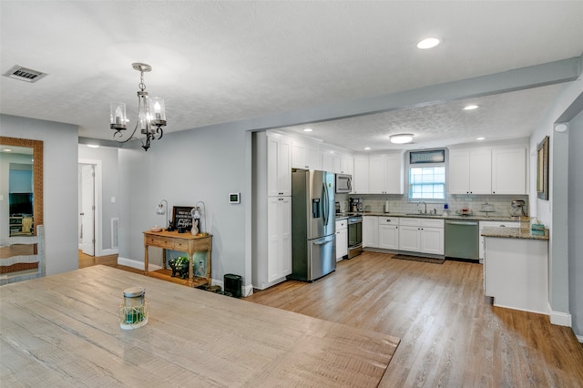 kitchen with appliances with stainless steel finishes, white cabinetry, a chandelier, and sink