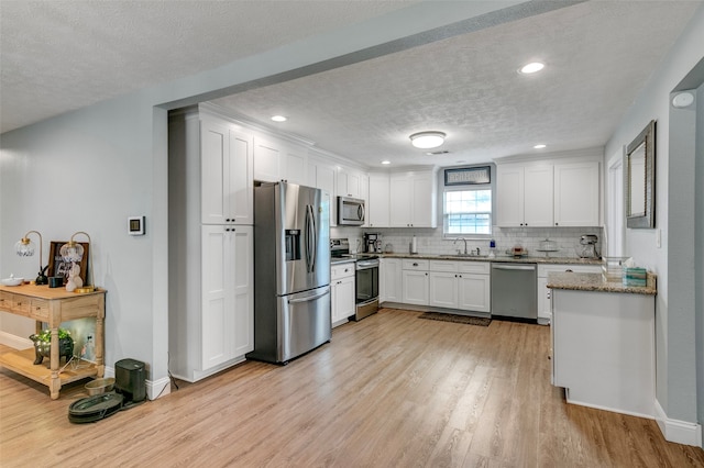 kitchen featuring light stone countertops, tasteful backsplash, appliances with stainless steel finishes, white cabinetry, and light wood-type flooring