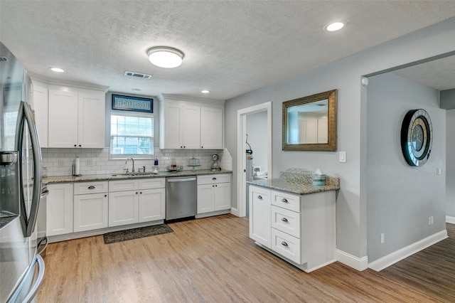 kitchen featuring white cabinets, stainless steel appliances, light wood-type flooring, and light stone counters