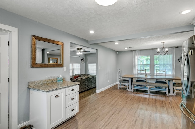 kitchen with white cabinets, light stone countertops, light hardwood / wood-style flooring, and ceiling fan with notable chandelier