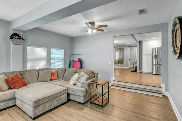 living room with light hardwood / wood-style floors, a textured ceiling, and ceiling fan