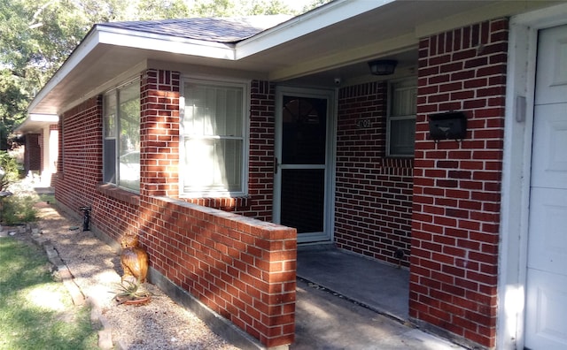 view of exterior entry featuring brick siding and roof with shingles