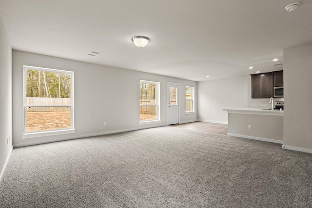 unfurnished living room with sink, carpet floors, and a wealth of natural light