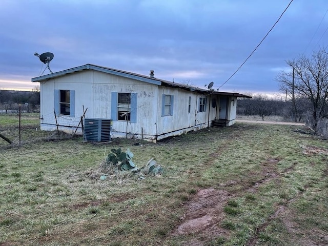 back house at dusk with a lawn and central AC