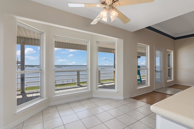 interior space with ceiling fan, a water view, a wealth of natural light, and light tile patterned flooring