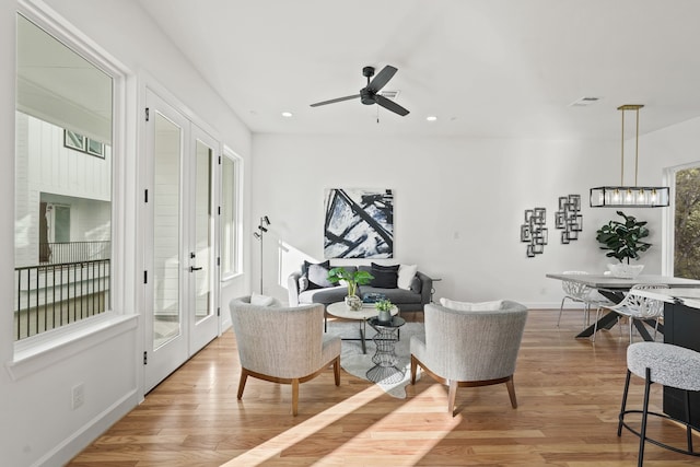 living area featuring french doors, light wood-type flooring, and ceiling fan with notable chandelier